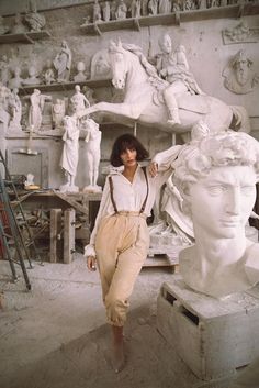 a woman standing next to a statue in a room filled with busts and statues