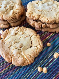 three peanut butter cookies sitting on top of a blue and yellow table cloth next to peanuts