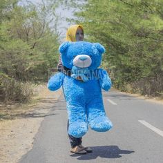 a person in a blue teddy bear costume is walking down the road with a large stuffed animal on his back