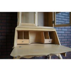 a wooden desk with two drawers and an open cabinet above it, against a brick wall