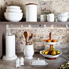 white dishes and utensils sit on shelves in front of a stone brick wall