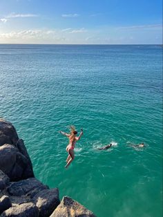 a woman jumping into the ocean from rocks in front of her and another person swimming