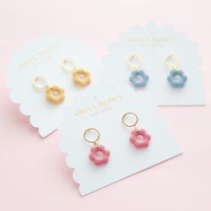 three pairs of earrings with donuts on them sitting next to each other in front of a pink background