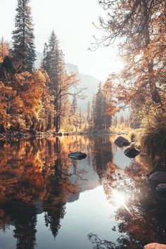 a lake surrounded by trees and rocks in the middle of autumn with sun shining on it