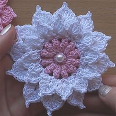 two crocheted flowers are being held by someone's hand on a table