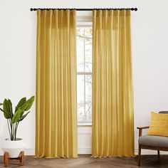 a living room with yellow curtains and a chair in front of a window that has a potted plant next to it