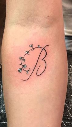 a woman's arm with a tattoo on it that says b and has flowers growing out of it