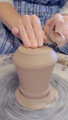 a woman is making a vase out of clay on a potter's wheel with her hands