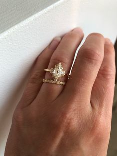 a woman's hand with a diamond ring on top of her finger, next to a white wall