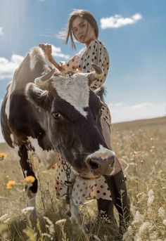 a woman is riding on the back of a cow in a field with wildflowers