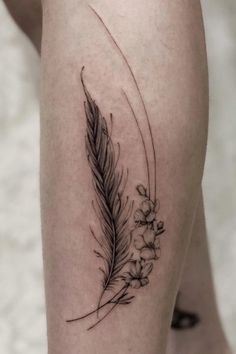 a woman's leg with a feather and flowers tattoo on the side of her thigh