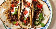 three tacos on a plate with sour cream and tomatoes