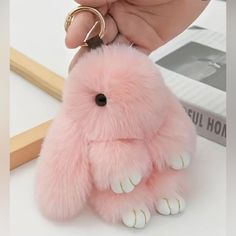 a hand holding a pink furry animal keychain