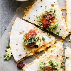 several quesadillas with guacamole and salsa on top, next to a bowl of guacamole