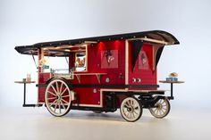 a red and black food cart with wheels on the front, sitting on a white surface