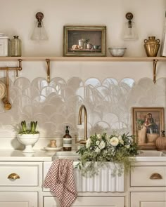 a kitchen with white cabinets and gold accessories on the shelves above it is a vase filled with flowers