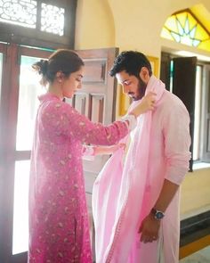 a man and woman standing next to each other in front of a window wearing pink clothing