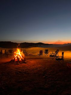 a campfire in the middle of a field with chairs around it at night time