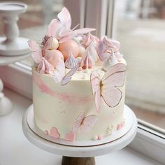 a white cake with pink butterflies and eggs on it sitting in front of a window