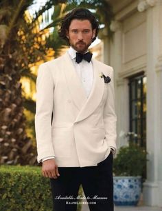 a man wearing a white tuxedo and bow tie standing in front of a building