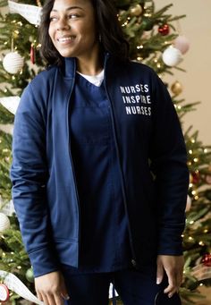 a woman standing in front of a christmas tree wearing a blue jacket with nurses inspire written on it