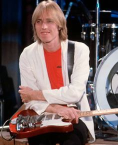 a man sitting on top of a wooden floor next to a drum kit and an electric guitar