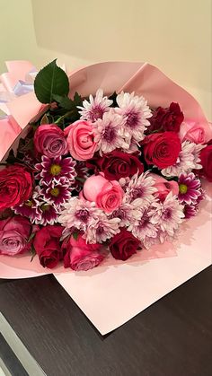 a bouquet of pink and red flowers sitting on top of a table next to a piece of paper