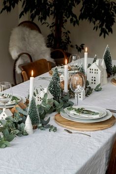 the table is set with candles, plates and greenery