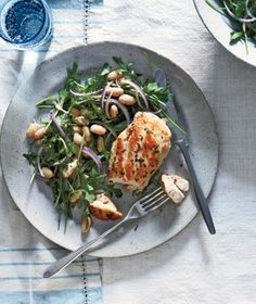 a white plate topped with chicken and salad next to a fork on a table cloth