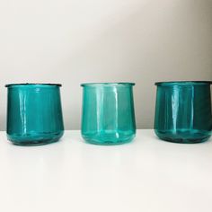 three teal glass jars sitting on top of a white table