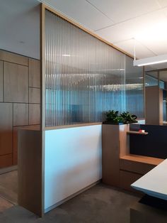 an office cubicle with glass partitions and wooden shelves on the wall, next to a planter