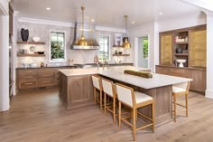 a large kitchen with wooden floors and white counter tops, gold pendant lights hanging from the ceiling