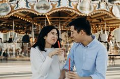 a man and woman standing next to each other in front of a merry go round