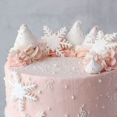 a pink frosted cake with white snowflakes on top and decorations around the edges