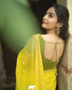 a woman in a yellow sari leaning against a wall and looking off to the side