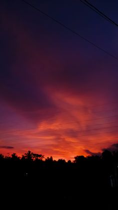 the sky is purple and orange as the sun goes down in the distance with power lines above it