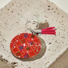 a red and pink keychain sitting on top of a cement block with a tassel