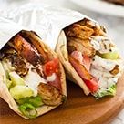 two burritos with meat, lettuce and tomatoes in wrappers on a cutting board