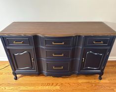 an old dresser has been painted black with gold hardware and is sitting on a hard wood floor