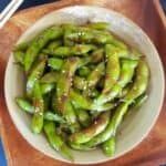 a white bowl filled with green beans on top of a wooden cutting board next to chopsticks