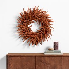 an orange wreath on a white wall next to a book shelf and vase with a candle