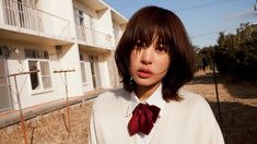 a young woman standing in front of an apartment building wearing a red bow tie and white shirt