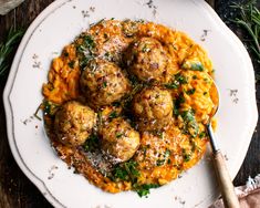 a white plate topped with meatballs covered in grated cheese and garnished with herbs