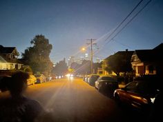 cars are parked on the street in front of some houses at night with city lights behind them