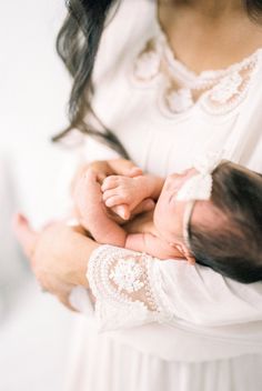 a woman holding a baby in her arms with white lace on it's sleeves