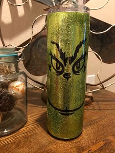 a green glitter tumbler sitting on top of a wooden table next to a glass jar