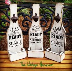 three wooden bottles with words on them sitting on top of a bench next to a fence