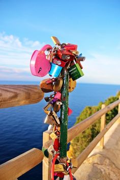 a bunch of locks attached to a wooden rail near the ocean with blue sky in background