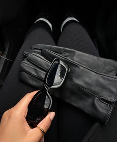 a person wearing black leather gloves and holding a cell phone in their left hand while sitting on a car seat