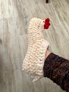 a hand holding a crocheted chicken on top of a wooden floor